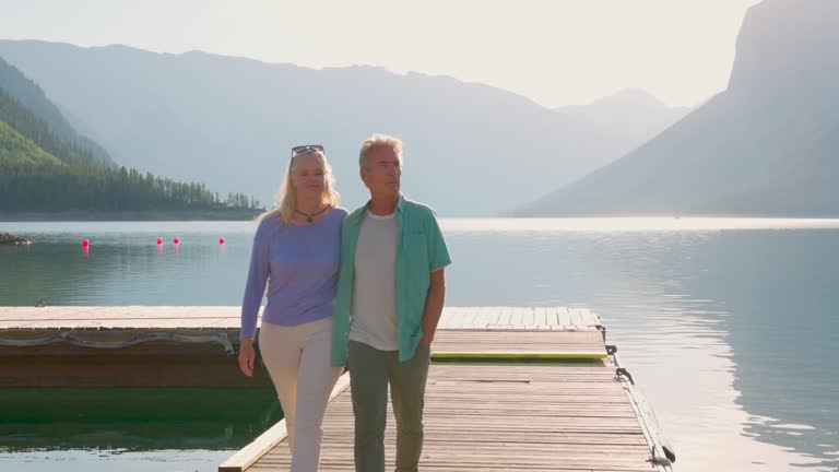 Senior couple enjoy walk along wooden lake pier