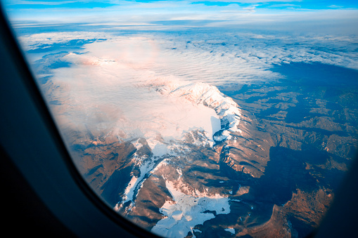 View out plane window on Mountain peaks with snow during the flight. Passenger Point of View out of Commercial Airplane Window on mountain range. Traveling above beautiful landscape. Copy space