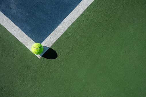 Tennis ball on the field line meaning it is not out. The ball is casting a dark shadow due to the morning sun