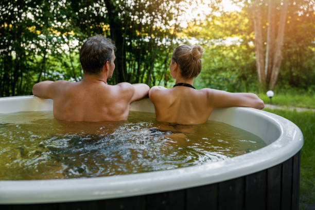 casal jovem relaxando junto na banheira de hidromassagem ao ar livre no forest resort. spa tratamento de natureza, escapadela romântica - couple hot tub spa treatment health spa - fotografias e filmes do acervo