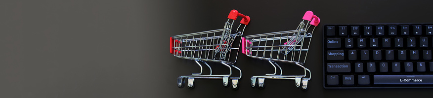 Specialized computer keyboard and two supermarket carts on a dark gradient background. The concept of e-commerce and remote online sales. Web banner. Gradient