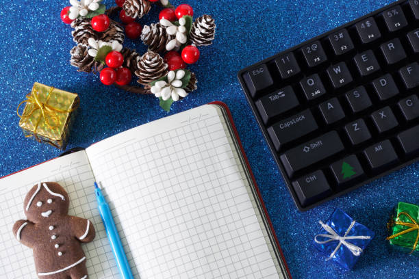 istock Computer keyboard, New Year and Christmas decorations, a gingerbread man and an open notebook on a sparkling blue background. Christmas and new year in the office. Corporate party invitation. 1497468620