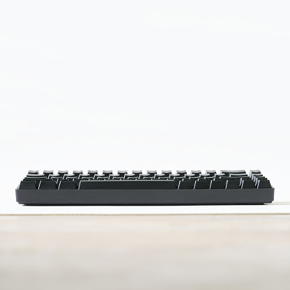 Black mechanical computer keyboard isolated on white and beige background. Small wireless keyboard for gadgets and computer. Gaming peripherals for digital gadgets. Copy space. Close-up