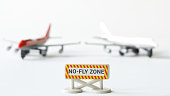 Sign with the inscription no-fly zone next to two toy passenger airliners on a white background. The concept of the ban on aircraft flights and the functioning of the no-fly zone. Selective focus.