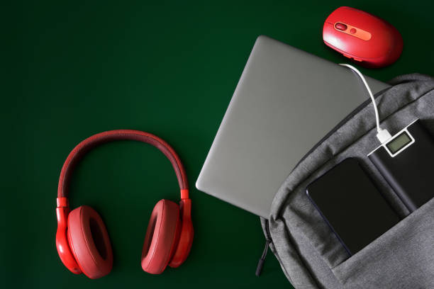 istock Trendy textile urban backpack with laptop, external battery - power bank, mobile phone, red headphones and computer mouse on green. Travel, trip and study with gadgets. Recharging devices. 1497468681