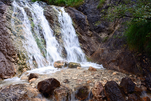 The flow of a small waterfall on the rock flows over the stones. Long exposure of the frame, the flow is blurred. Natural background of the surrounding environment