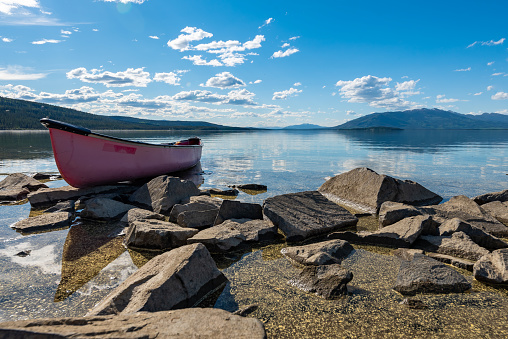 Lake side views on a perfect blue sky day with mountains & clouds reflecting in water. Red canoe in foreground taken in northern Canada, Yukon Territory.