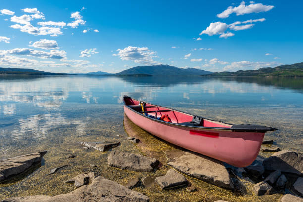 Lake side views on a perfect blue sky day with mountains & clouds reflecting in water. Red canoe in foreground taken in northern Canada, Yukon Territory.