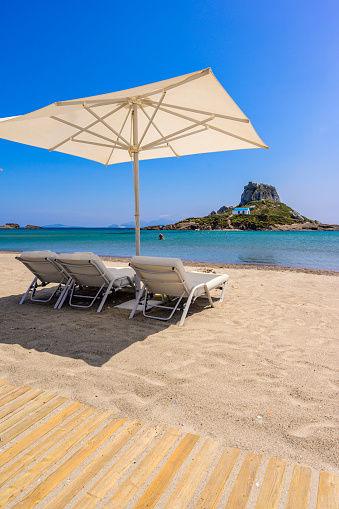 Deck chair and umbrella on beautiful Agios Stefanos Beach in front of Kastri island - historical ruins and paradise scenery at coast of island Kos, Greece