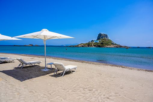 Deck chair and umbrella on beautiful Agios Stefanos Beach in front of Kastri island - historical ruins and paradise scenery at coast of island Kos, Greece