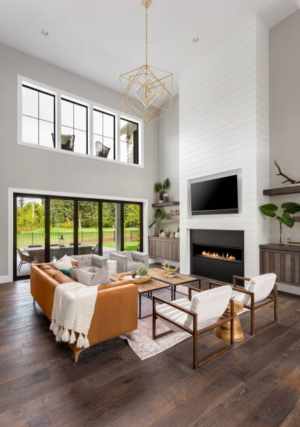 Beautiful living room interior with hardwood floors and fireplace in new luxury home. Features floor to ceiling fireplace surround, wall of windows, and elegant furnishings. stock photo
