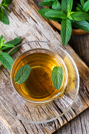 Cup of mint tea with fresh green mint leaves on rustic table, healthy herbal hot drink