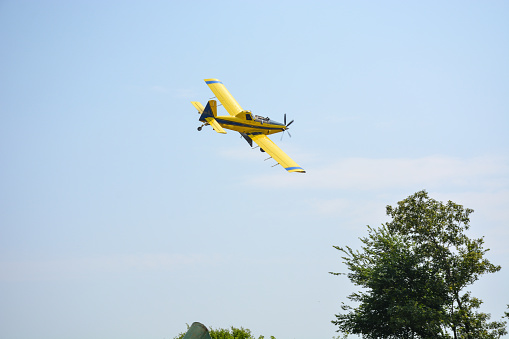 A crop-dusting plane flies away ready to bank around and continue dusting a field.