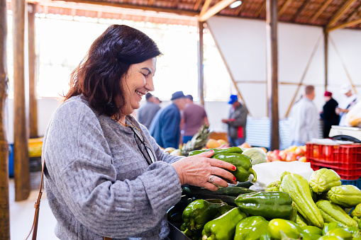 Mature Brazilian woman choosing and buying vegetables at the farmers market.