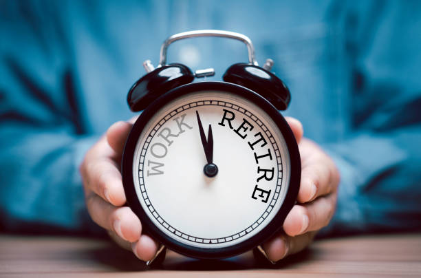 仕事から退職までの時計回りのカウントダウンを持つ黒い目覚まし時計を持つ実業家。 - リタイアメント ストックフォトと画像