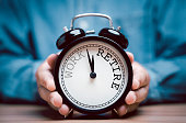 Businessman holding black alarm clock with clockwise countdown from work to retirement.