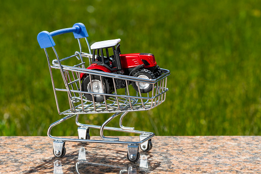 Miniature tractor in a shopping cart from a supermarket on a background of grass