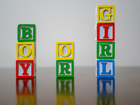 BOY OR GIRL spelled out in colorful, wooden toy blocks.  The blocks reflect of the table they are stacked on.