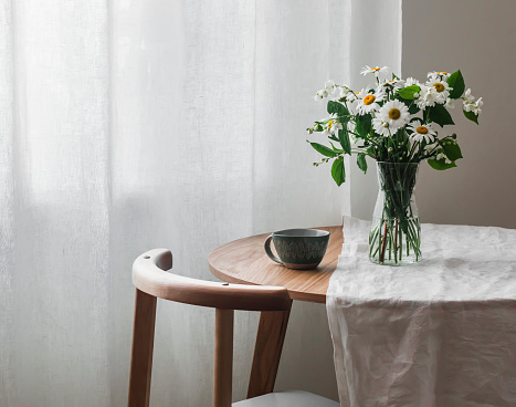 Slow morning - a cup on a wooden table with a white tablecloth and a vase with daisies and jasmine