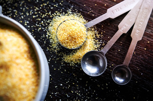 A kitchen countertop with a measuring bowl, spoons, and yellow grains