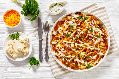 Bacon Mozzarella Feta Cheddar Cheese Fries with ranch dressing and parsley on white dish on wood table, american cuisine, horizontal view from above, flat lay