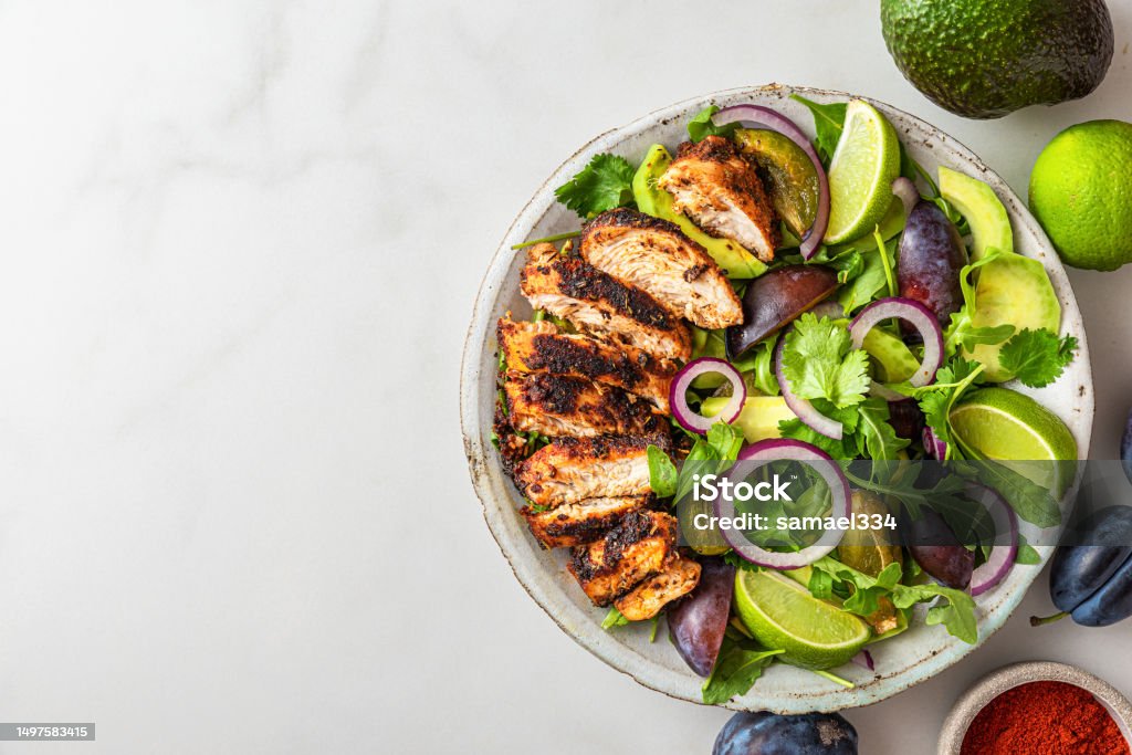 Grilled chicken fillet salad with arugula, avocado, plums, paprika, onion and lime in a plate on white background Grilled chicken fillet salad with arugula, avocado, plums, paprika, onion and lime in a plate on white background. Top view with copy space. Healthy diet food Healthy Eating Stock Photo