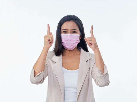 Woman with protective mask pointing at something on white background. Space for text