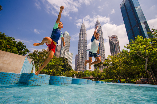 Boys jumping and enjoying in pool that is in front of Petronas Twin Towers of Kuala Lumpur, Malaysia.
