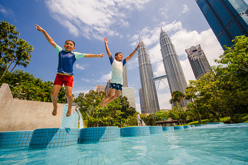 Boys jumping and enjoying in pool that is in front of Petronas Twin Towers of Kuala Lumpur, Malaysia.