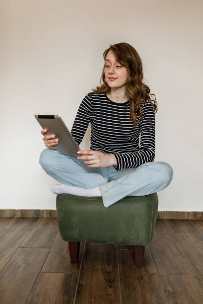 istock Young woman sitting on a cozy, little green stool and using digital tablet 1497590225