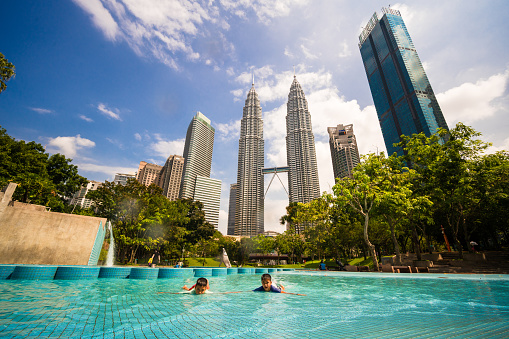 Boys swimming and enjoying in pool that is in front of Petronas Twin Towers of Kuala Lumpur, Malaysia.