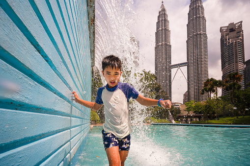 Boys running and enjoying under waterfall  in front of Petronas Twin Towers of Kuala Lumpur, Malaysia.