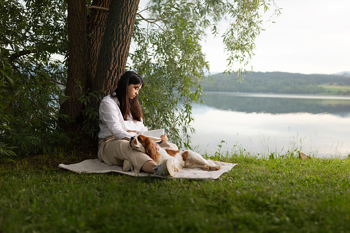 Young woman reading book under tree her dog