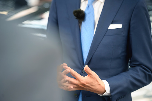 Midsection of a politician or businessman standing and speaking in front of reporters at a press conference