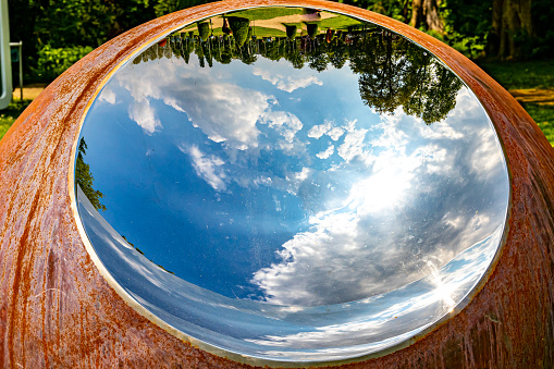 Reflection in a round mirror of blue sky with white clouds and trees with green foliage in background, sunny spring day in dutch castle garden backyard, South Limburg in the Netherlands
