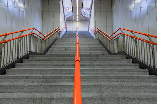 An empty stairway with orange bannister is leading up to the exit of a subway station in Vienna.\nCanon EOS 5D Mark IV, 1/4, f/10, 24 mm.