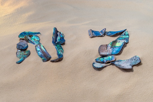 Broken pieces of beautiful Paua shell spell the word NZ on a sandy beach in New Zealand.