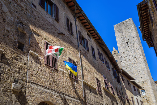 San Gimignano, Italy - April 2, 2023: Walls of the city of San Gimignano with flags on the facade. The Town of Fine Towers. Is typical Tuscan medieval town in Italy. Province of Siena, Tuscany.