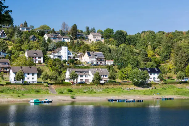Houses at the beach in Rurberg at Lake Rursee with perfect blue sky in summer in the Eifel, Germany.