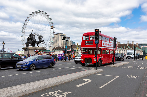 London, England; 06/06/2023: English double-decker bus crossing Westminster bridge with the ferris wheel \