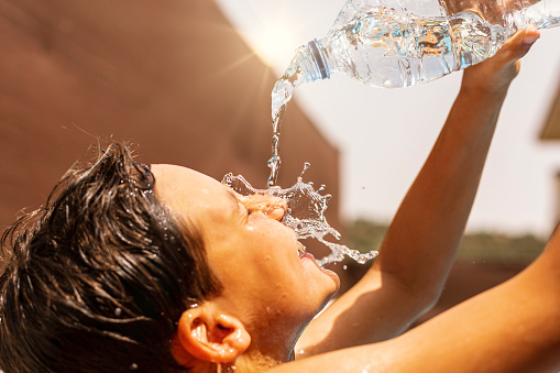 Young man throwing water from the bottle over his head due to heat wave in summer