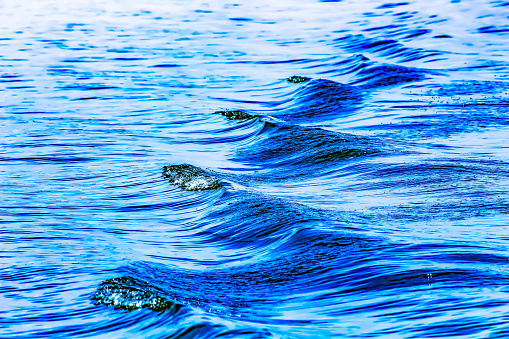The ripples coming from the wake of a boat represent the abstract flow of data and time.  This is an monochrome blue abstract background image.