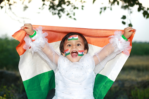 Cheerful 2-3 years girl raised hands and holding Indian flag in hand, celebrating Independence day, India.