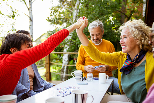 Smiling Mature females greeting high five while sitting and playing game with friends outside. Women happy for winning the card game