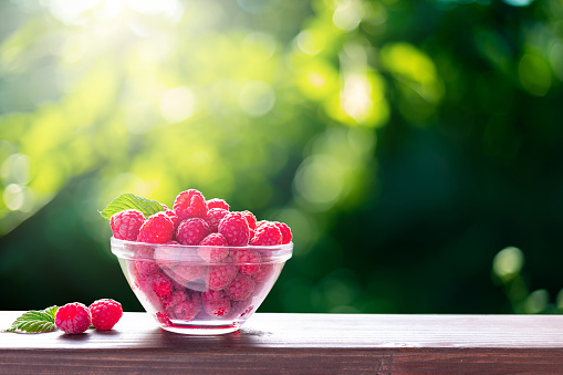 Summer harvest of ripe raspberries in the glass bowl on a wooden railing of the terrace.