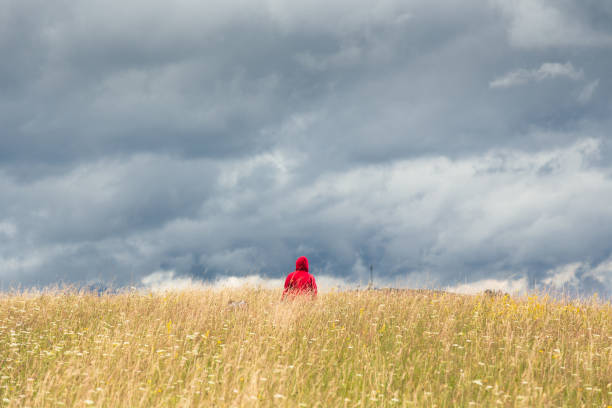 istock A lonely man in a red hoodie, standing atop a high grass mountain hill under a dramatic cloudy sky and enjoying tranquility and solitude. 1497619025