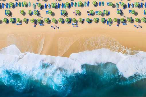 Aerial View of sandy beach with colorful umbrellas and blue water  with waves on sunny day, summer vacation concept. Travel background top view