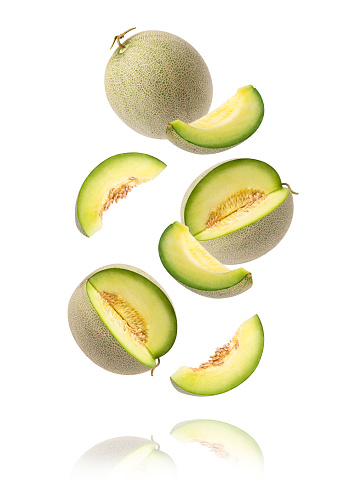Green cantaloupe melon with cut slice flying in the air isolated  background.