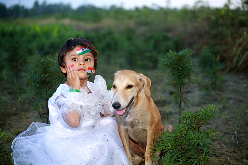 Baby girl sitting with pet dog outdoors in the agricultural field on independence day.