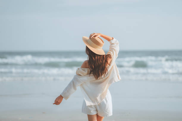 concetto di vacanza estiva sulla spiaggia, giovane donna con il cappello che si rilassa con le braccia alzate alla testa godendo della vista dell'oceano della spiaggia nella calda giornata estiva, spazio di copia. - beach women joy sand foto e immagini stock